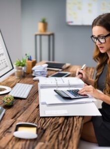 A businessperson's hand is shown in close-up as they calculate an invoice at their workplace.
