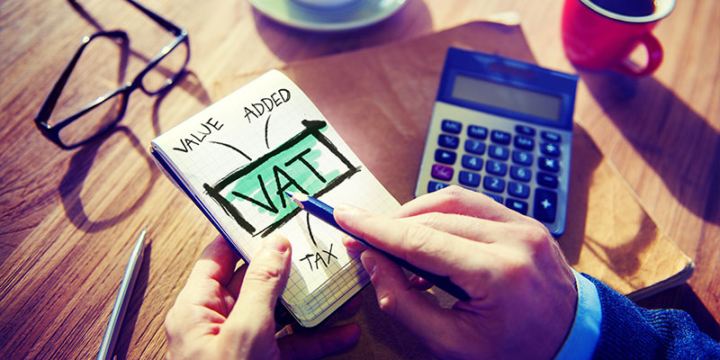 A Man's hand pointing out Value Added Tax (VAT) text in a notepad