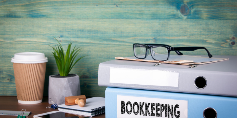 The concept of bookkeeping is illustrated by binders and some stationery items on a desk in the office.